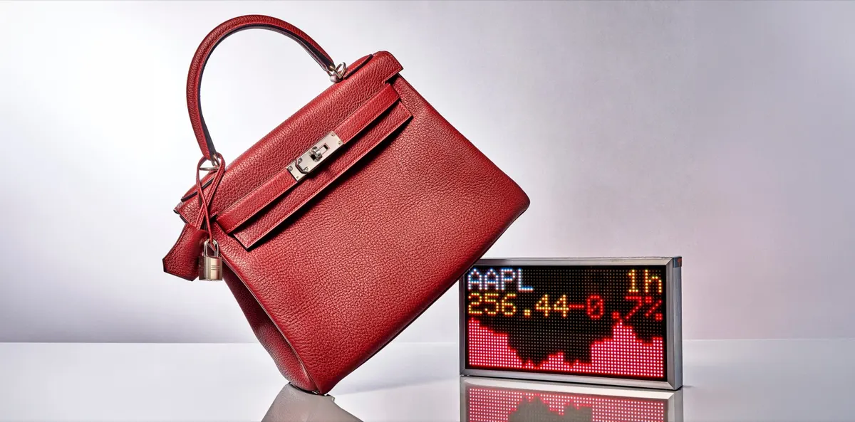 A red Hermès Birkin handbag beside a stock ticker